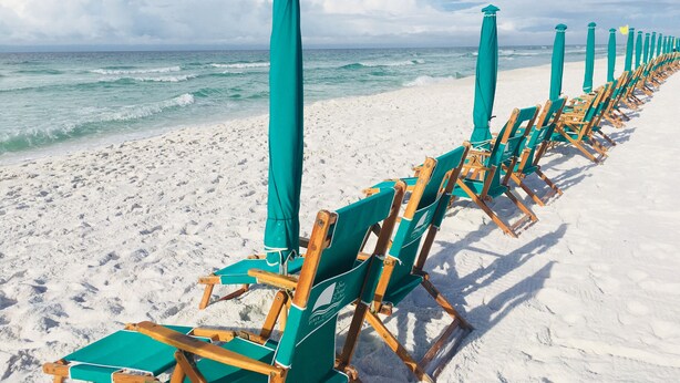 Une plage bordée de rangées de chaises longues en bois et de parasols assortis, alignés le long du rivage.