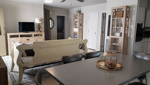 Een eethoek met een tafel, stoelen, een bank, een televisie en een keuken met kastjes en een plank.
