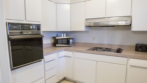 Een keuken met witte kasten, een ingebouwde oven, een magnetron en een rvs afzuigkap.