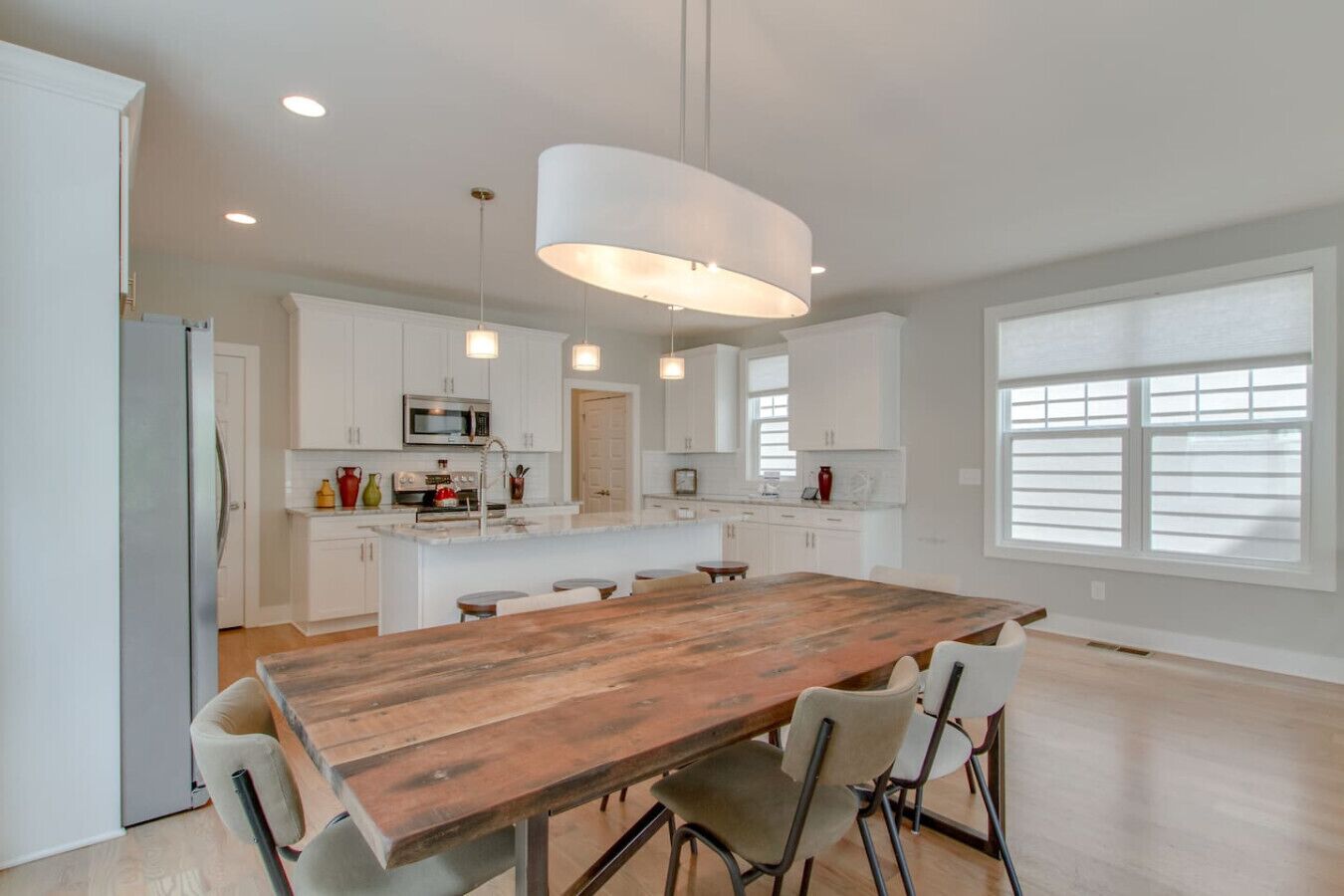 A spacious kitchen with white cabinets, a wooden island table, and pendant lighting.