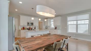 A spacious kitchen with white cabinets, a wooden island table, and pendant lighting.