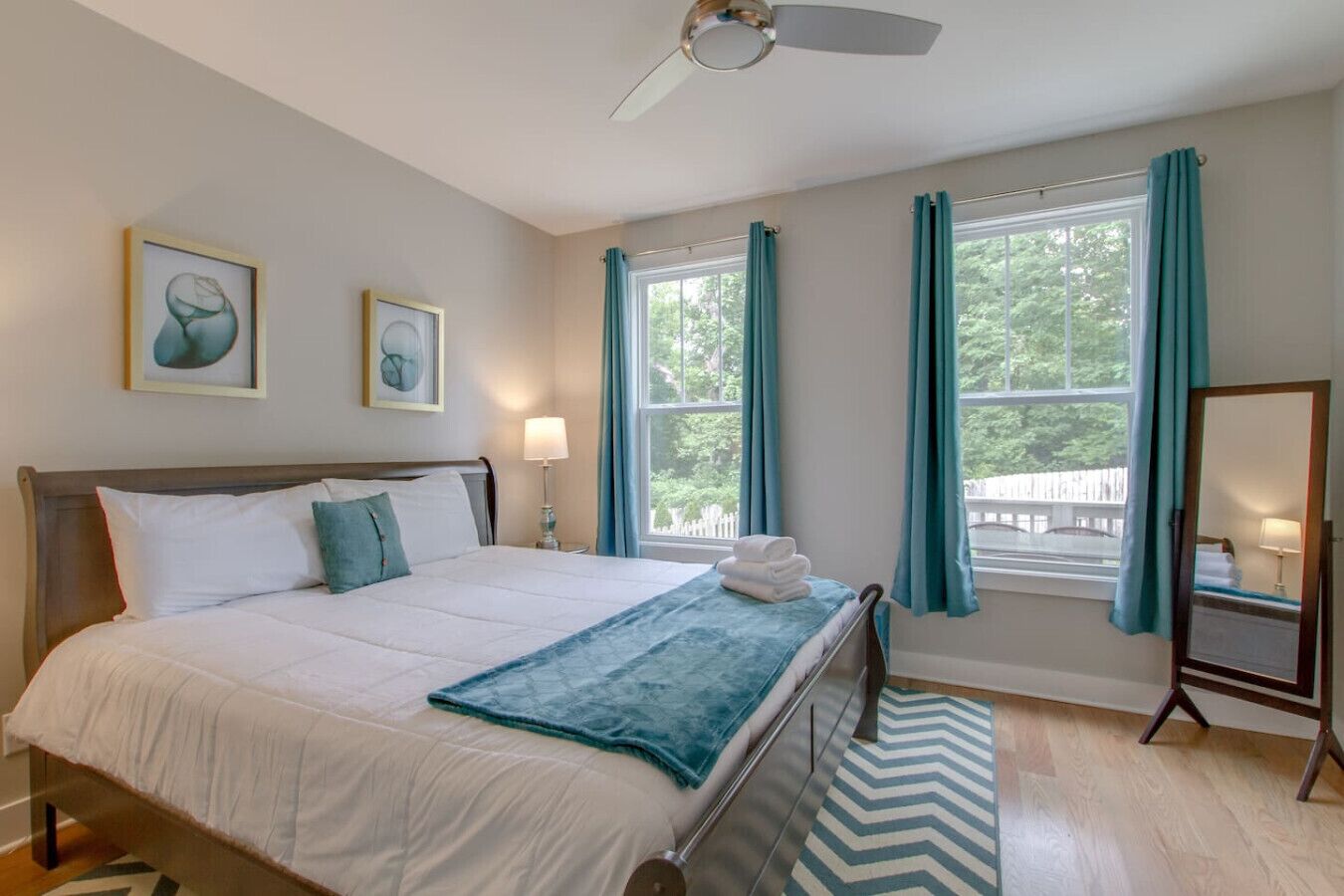 A bedroom with a bed, two bedside tables, a ceiling fan, a window with curtains, and artwork on the wall.