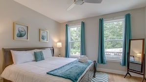Ein Schlafzimmer mit einem Bett, zwei Nachttischen, einem Deckenventilator, einem Fenster mit Vorhängen und Kunstwerken an der Wand.