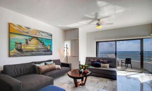 Ein Wohnzimmer mit einem großen Gemälde, einem Deckenventilator und Meerblick von einem Balkon aus.