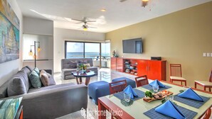 A spacious living area with a balcony, a dining table set with blue napkins, and a TV mounted on the wall.