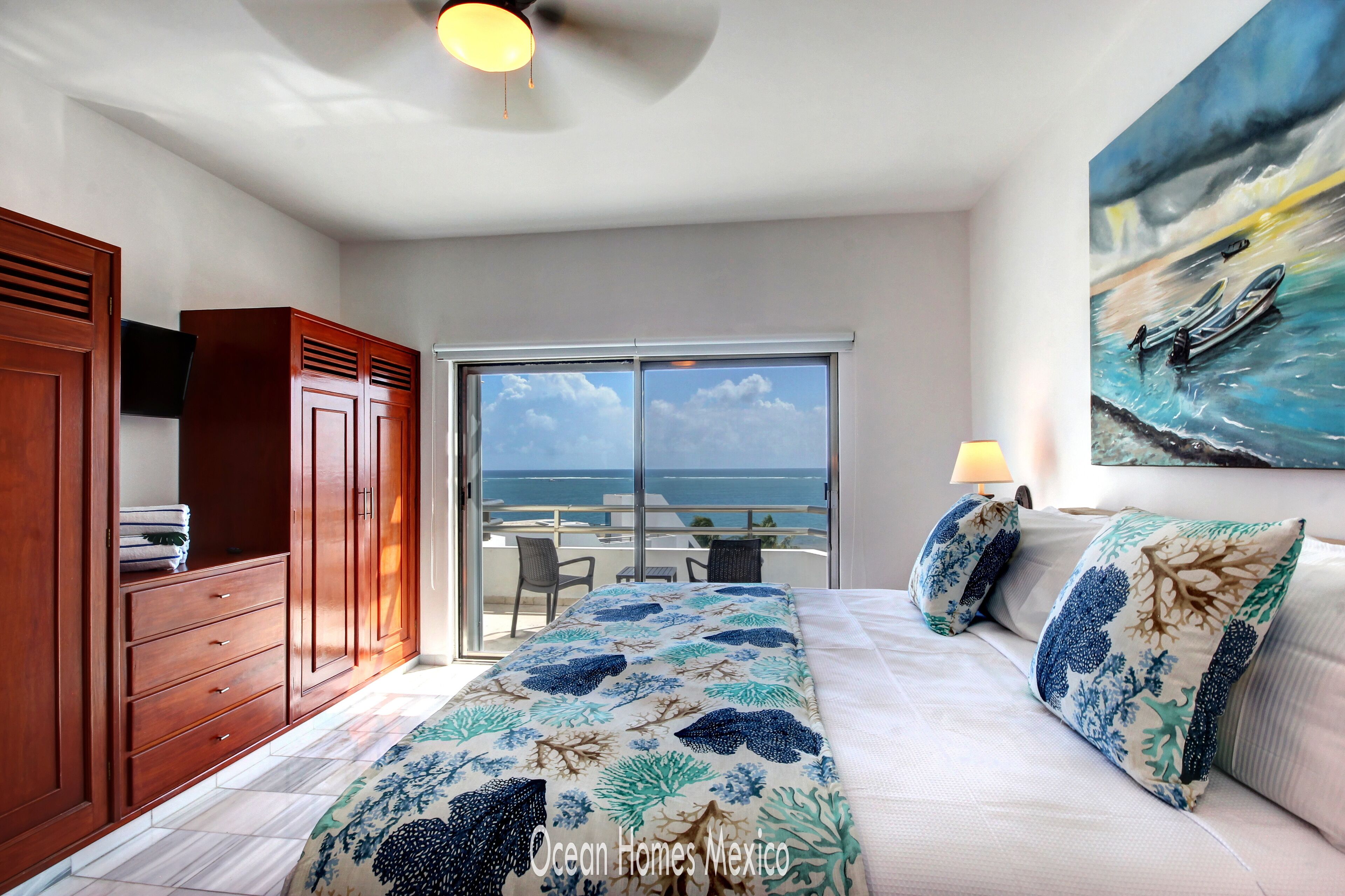 A bedroom with a bed, a large window, and a view of the ocean.
