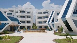 A modern hotel with a symmetrical facade, multiple balconies, and a central courtyard with lounge chairs.