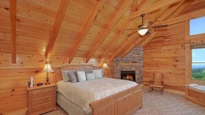 Une chambre située dans un chalet en rondins, avec un grand lit, une cheminée en pierre et une vue sur l’extérieur.