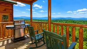 Une terrasse en bois avec un barbecue et des chaises, donnant sur un paysage boisé.