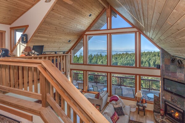 A spacious loft-style room with large windows offering a view of a forested area.