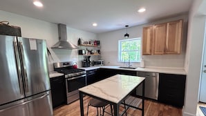 A modern kitchen with stainless steel appliances, wooden cabinets, and a large window providing natural light. - Modern Designer Beach House 1 mile to the beach! Pet-friendly & bright (Sawyer)