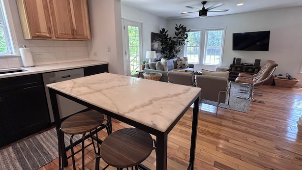 A modern kitchen with a marble countertop, wooden cabinets, and a dining area with bar stools. - Modern Designer Beach House 1 mile to the beach! Pet-friendly & bright (Sawyer)