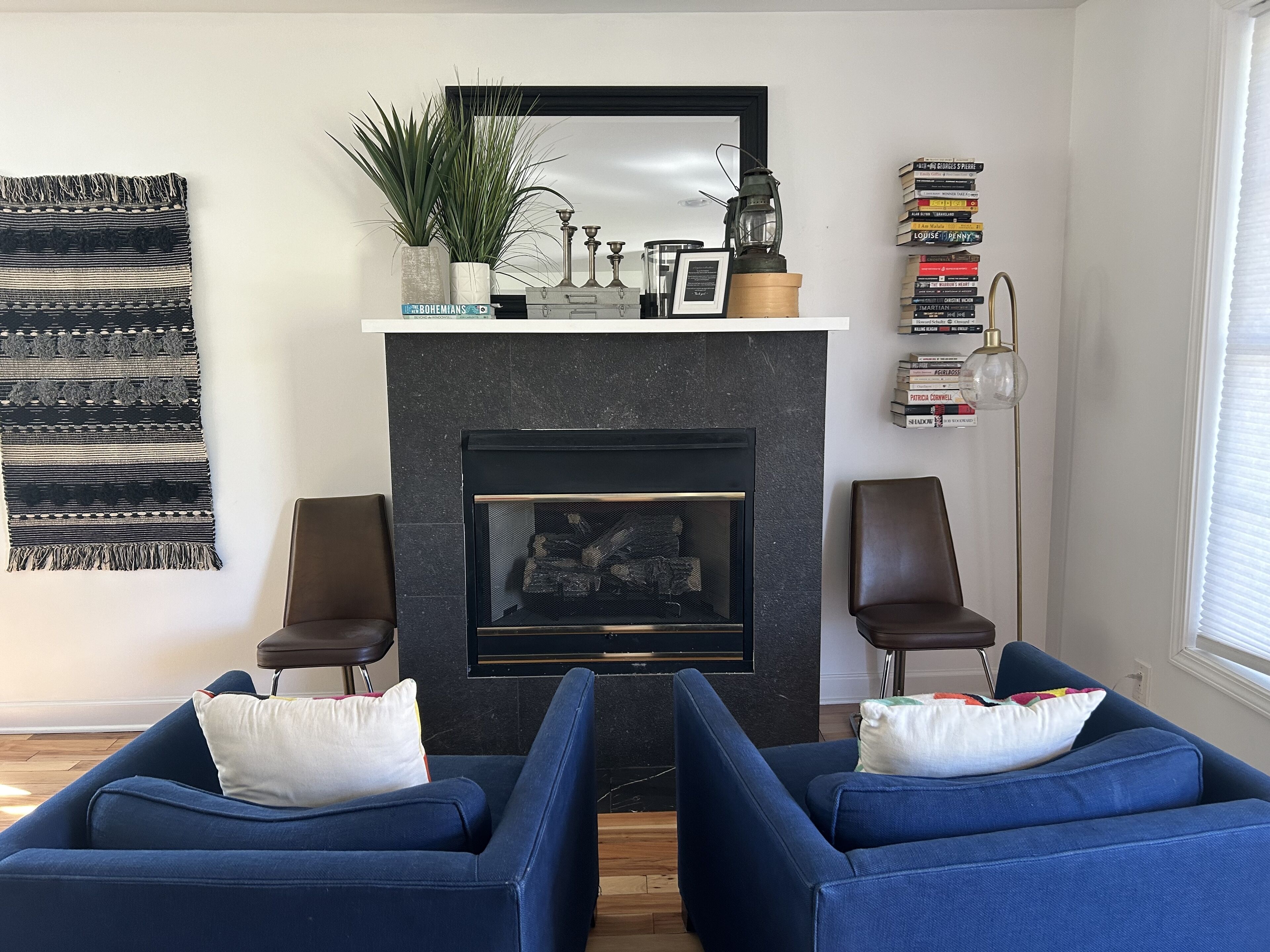 A living room with a fireplace, two blue sofas, a mirror, a plant, and a bookshelf.