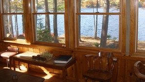 A room with large windows overlooking a lake, wooden furniture, and a view of trees.