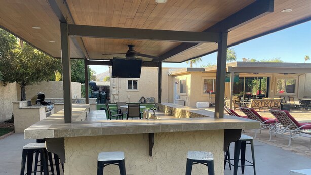 An outdoor bar area with a stone countertop, bar stools, and a ceiling fan. - 8 Bedrooms, 12 beds, pool, hot tub,putting green, pool table, ping pong, bbq (Phoenix)