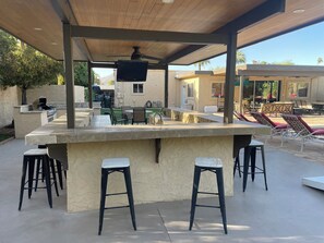 Un espace bar extérieur doté d’un comptoir en pierre, de tabourets de bar et d’un ventilateur de plafond.