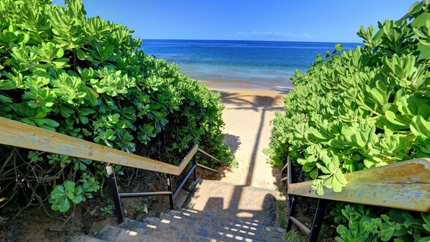 A staircase leading to a beach with clear blue water and a sandy path.