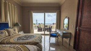 Une chambre d’hôtel équipée d’un lit, d’un bureau, d’une chaise et offrant une vue sur la mer grâce à une porte-fenêtre coulissante.