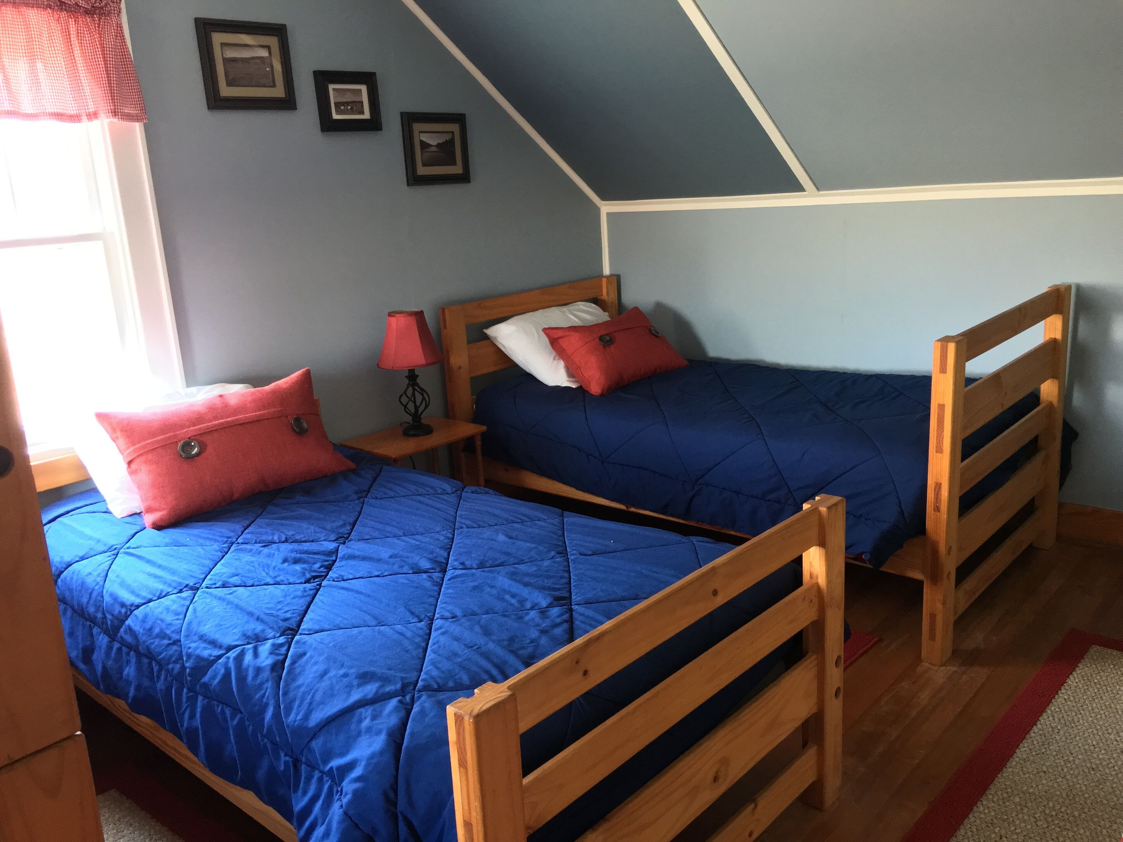A bedroom with two wooden bunk beds, a nightstand with a lamp, and three framed pictures on the wall.