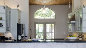 Una cocina con techo de madera, armarios blancos, un ventanal grande y tres taburetes de bar.