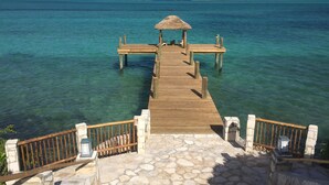 Un muelle de madera que lleva a una estructura de techo de paja sobre aguas turquesas cristalinas.