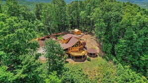 A large wooden cabin surrounded by dense forest, with multiple decks and a small gazebo. - Luxurious, Secluded Cabin, with Gazebo Covered Hot-tub + Amazing View (Blue Ridge)