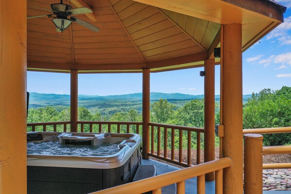 A hot tub under a wooden gazebo with a view of green hills.