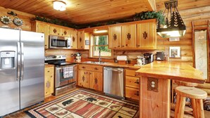 A cabin-style kitchen with wooden cabinets, stainless steel appliances, a wooden bar, and a large window. - Luxurious, Secluded Cabin, with Gazebo Covered Hot-tub + Amazing View (Blue Ridge)