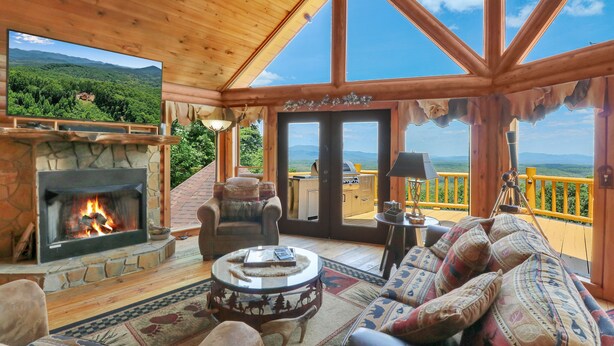 A cozy cabin interior with a stone fireplace, comfortable seating, and a large window offering a scenic mountain view. - Luxurious, Secluded Cabin, with Gazebo Covered Hot-tub + Amazing View (Blue Ridge)