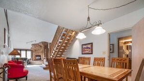 Un espace repas avec une table et des chaises en bois, un escalier et une cheminée.