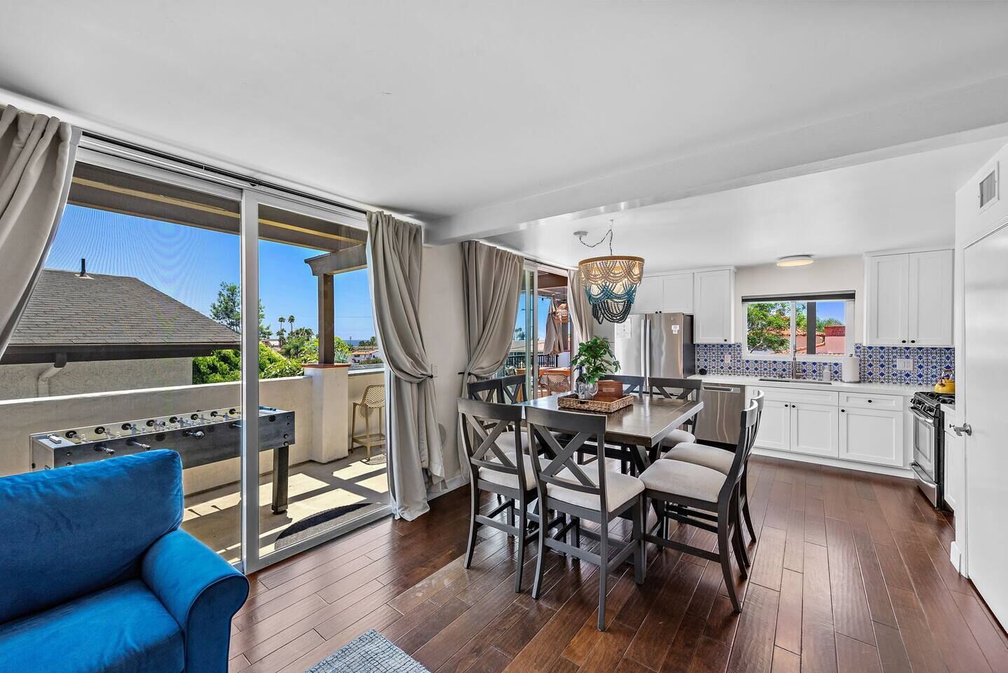 A modern kitchen with white cabinets, a dining area with a table and chairs, and a balcony with a blue chair.