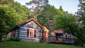 A rustic cabin with a stone chimney, a red door, and a wooden deck.