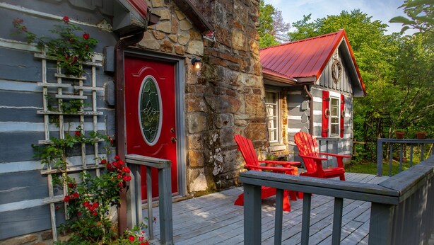 A wooden deck with red Adirondack chairs and a stone building with a red door.