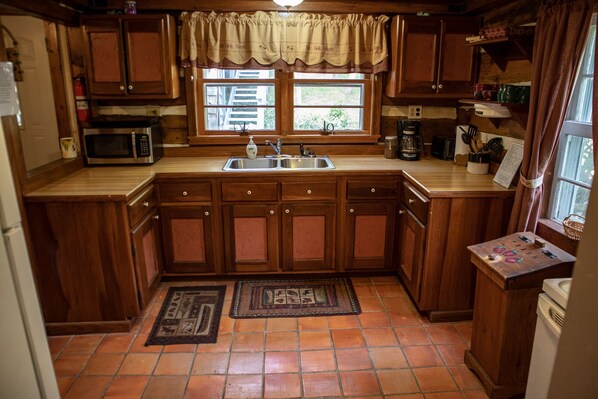 A compact kitchen with wooden cabinets, a stainless steel sink, a microwave, and a coffee maker.
