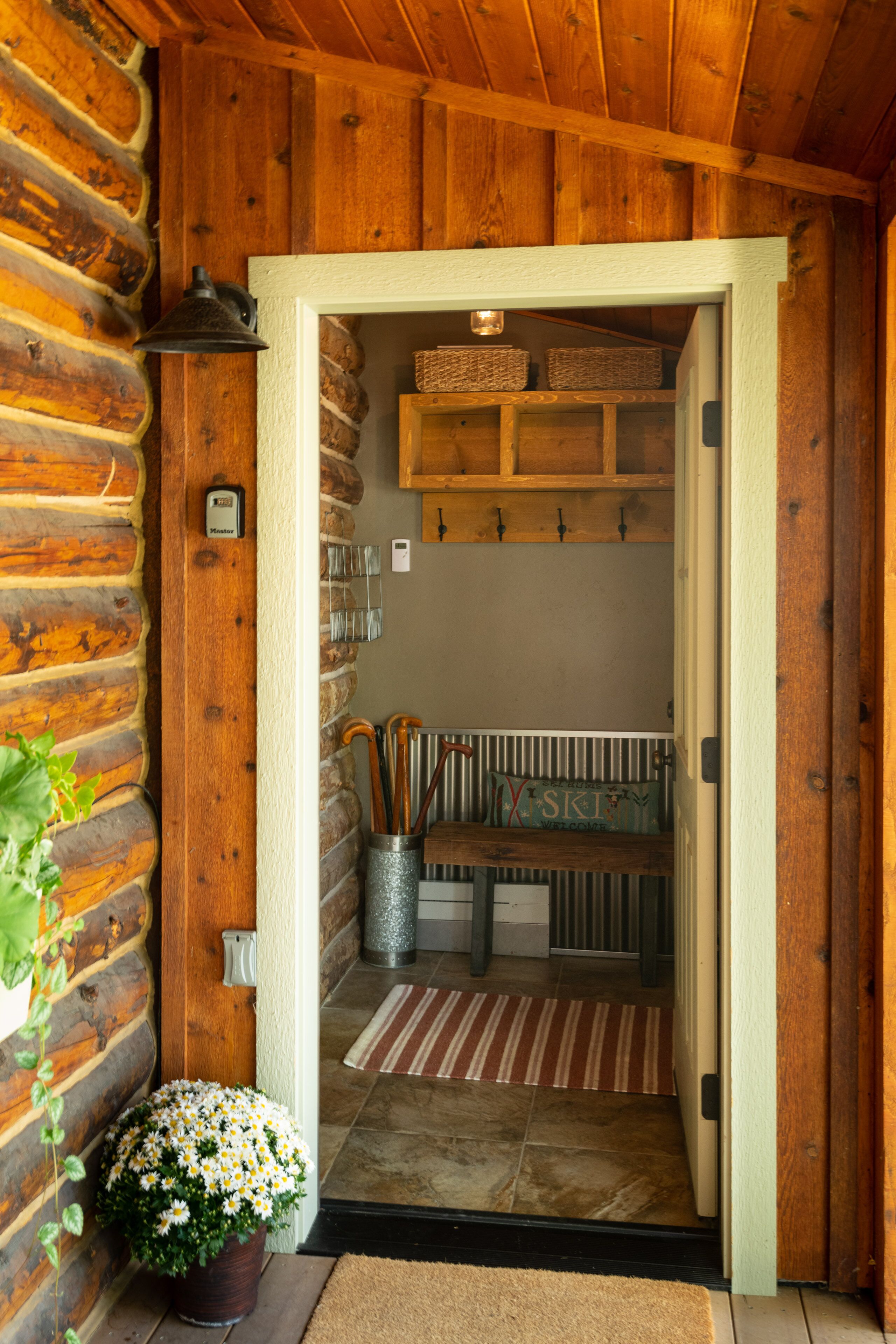 L’intérieur d’un chalet en bois présente une entrée accueillante, un petit coin salon avec des coussins et une plante en pot près de la porte.