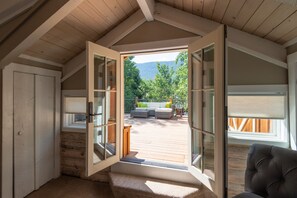 Une pièce dotée d’un plafond en bois et d’une grande porte ouverte donnant sur une terrasse extérieure avec un canapé et des coussins.