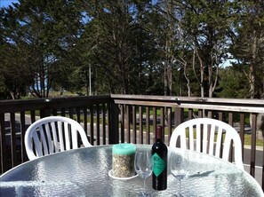 A round glass table with a bottle of wine and two empty wine glasses on a deck with white chairs. - Westside 3 BR + loft  Overlooks Natural Bridges Beach. Great for Families! (Santa Cruz)