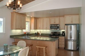 A modern kitchen with wooden cabinets, stainless steel appliances, and a glass island. - Westside 3 BR + loft  Overlooks Natural Bridges Beach. Great for Families! (Santa Cruz)
