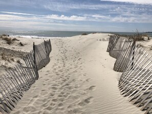 Un sentier de sable bordé de clôtures en bois de chaque côté, qui mène à l’océan.