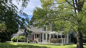 Ein zweistöckiges Haus mit überdachter Terrasse, umgeben von üppiger Vegetation und Bäumen.