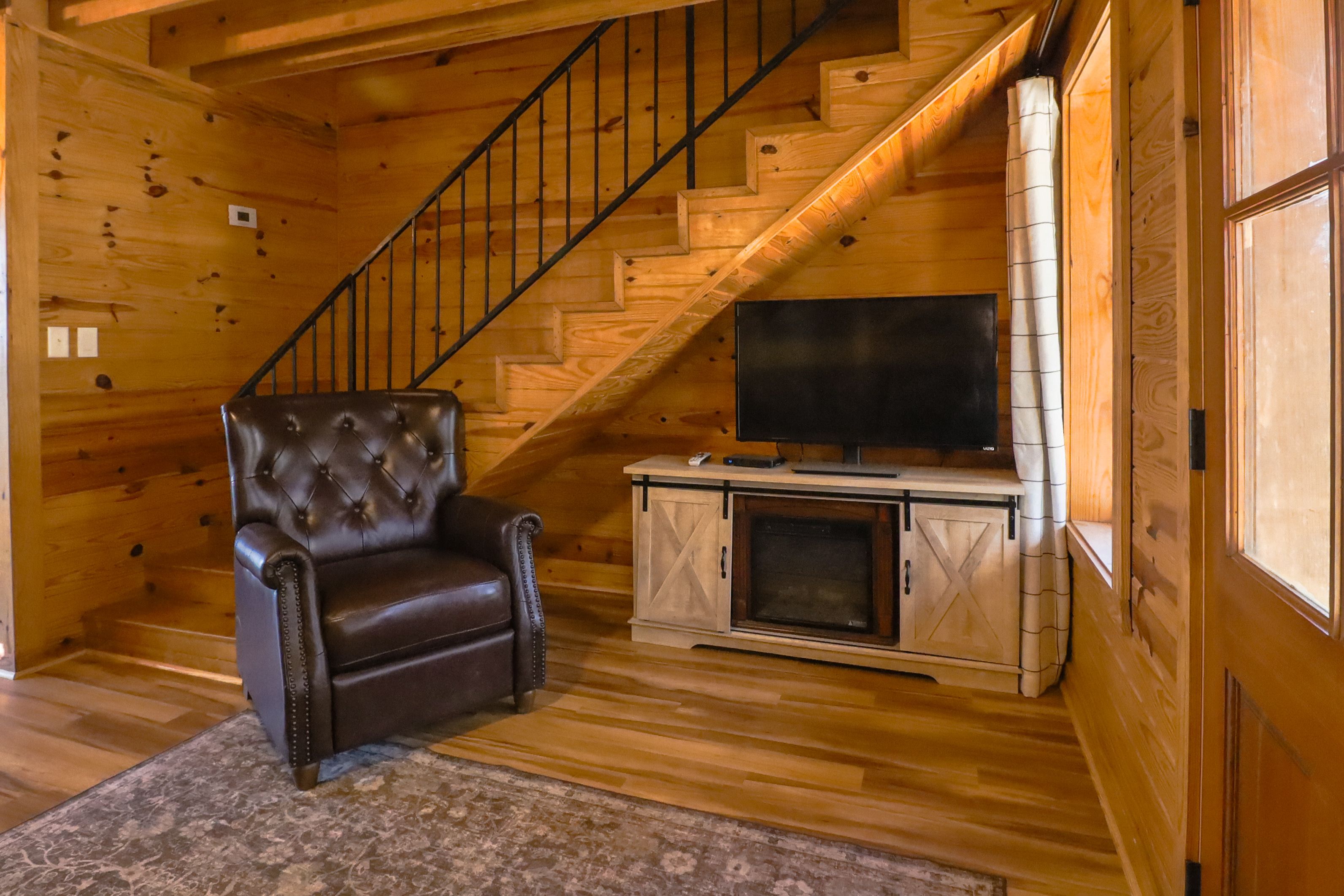 A wooden interior with a leather armchair, a flat-screen TV, and a fireplace.