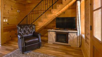 A wooden interior with a leather armchair, a flat-screen TV, and a fireplace.