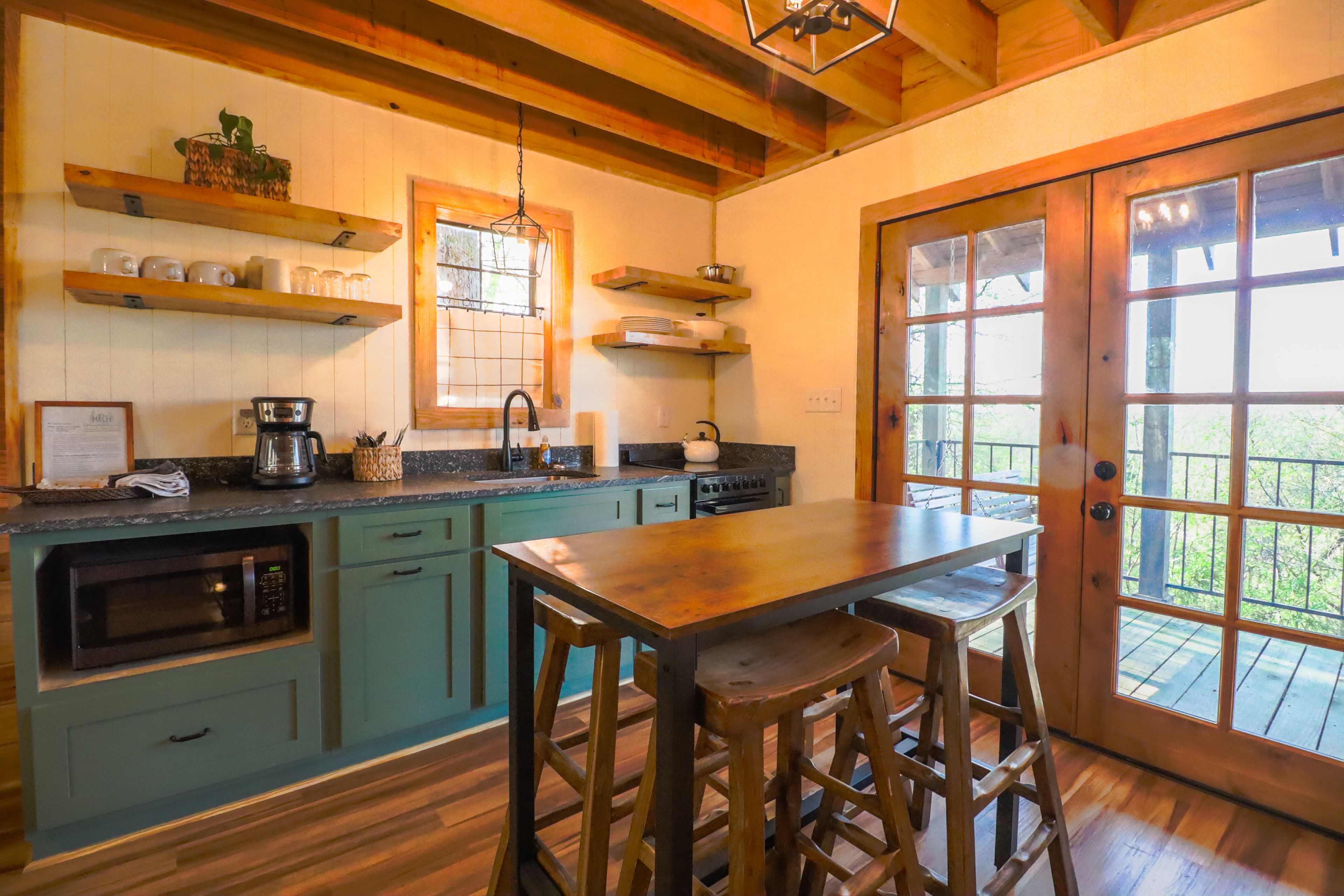 A kitchen with wooden beams, a bar stool, a coffee maker, and a window with a view.
