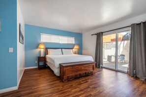 Ein Schlafzimmer mit einem großen Bett, zwei Nachttischen mit Lampen, einer hölzernen Bank und einer Schiebetür zu einem Außenbereich.