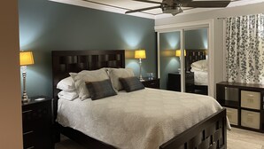 Une chambre à coucher comprenant un lit, deux tables de chevet avec des lampes, un ventilateur de plafond, un miroir et une armoire.