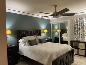 Relax in a serene bedroom with a dark wood headboard bed, a large mirror, and a ceiling fan for ventilation.