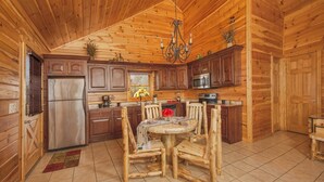 Interior de una cabaña de madera con comedor, cocina y un ventanal grande.