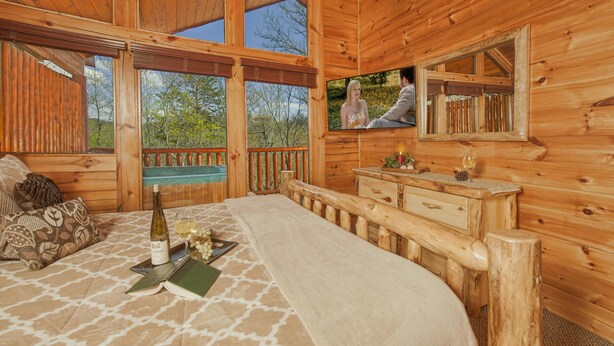 Un dormitorio de cabaña de madera con cama, cómoda, espejo y ventana con vistas a un bosque.