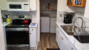 A compact kitchen with white cabinetry, a stainless steel stove, a microwave, a dishwasher, and a sink with a metal strainer. - Suttons Bay-Pet Friendly-Walk to Brewery, beach, town, shops (Suttons Bay)