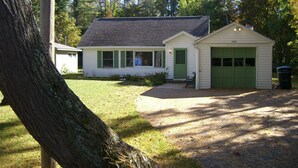 A two-story house with a green garage door, a front porch, and a large tree in the foreground. - Suttons Bay-Pet Friendly-Walk to Brewery, beach, town, shops (Suttons Bay)